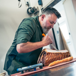Metzgermeister Herbert Waldinger schneidet ein Stück hochwertiges Fleisch in der Metzgerei präzise mit einem Messer zu.