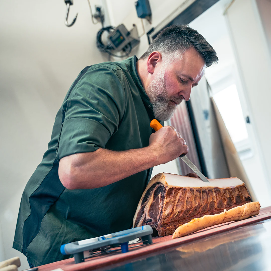 Metzgermeister Herbert Waldinger schneidet ein Stück hochwertiges Fleisch in der Metzgerei präzise mit einem Messer zu.